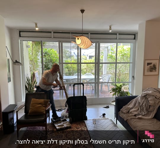 אדם עובד על תריסים בחדר מגורים עם חלון גדול